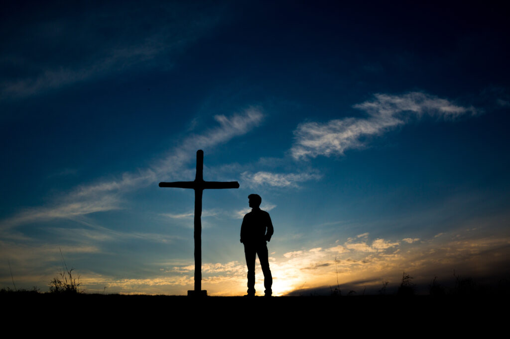 teenage boy silhouetted next to a cross